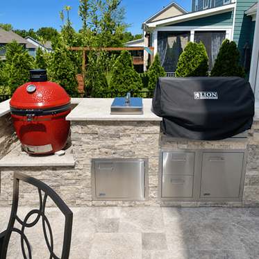 Outdoor kitchen with red kamado grill, built-in Lion gas grill, and travertine patio in Charlotte NC