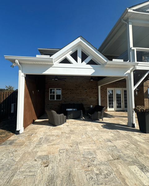 Custom covered patio with gabled roof, outdoor seating, and stone tile flooring—perfect for gatherings in Charlotte backyards.