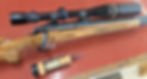 Wooden rifle with black scope on red surface, next to an orange and black screwdriver. No visible text, detailed wood grain.