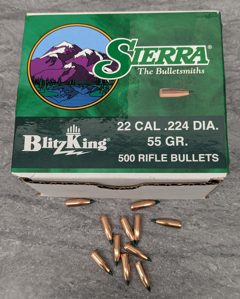 Box of Sierra BlitzKing 22 cal rifle bullets on gray surface. Green box with mountain logo and text "500 RIFLE BULLETS, 55 GR". Bullets scattered.