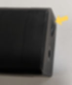 Close-up of a black rectangular object with a yellow arrow pointing to a hole on its side, set against a plain background.