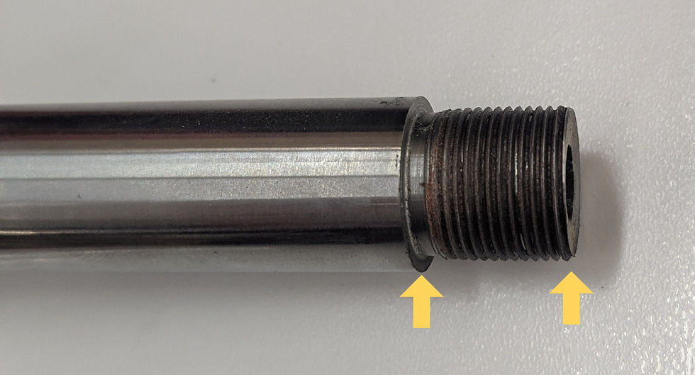 Close-up of a metallic threaded rod on a white surface with two yellow arrows pointing at the threads, highlighting details.