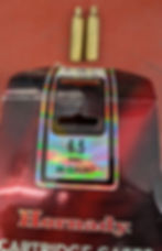 Two bullet casings on a red surface next to Hornady cartridge box. Text reads "6.5 PRC 50 COUNT" with a holographic label.