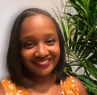 Alexis Marie standing in front of a grey wall with a plant behind her