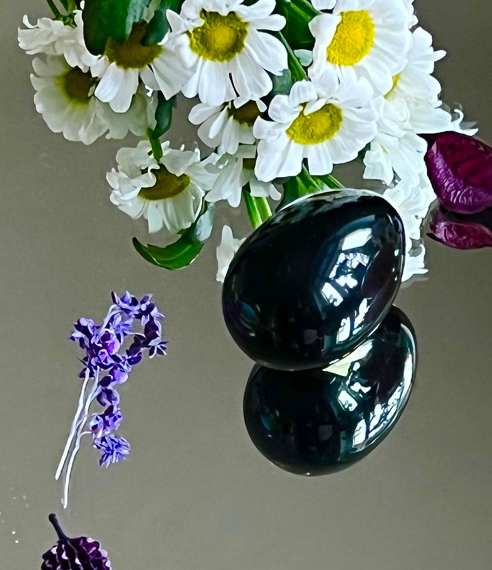 schwarzes Yoni-Ei Obsidian liegt auf einem Spiegel und ist von weißen und lila Blüten umgeben