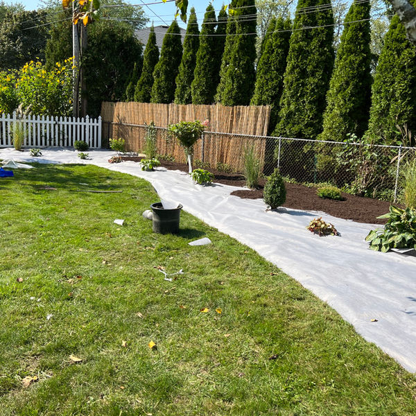 A landscape installation underway in Amherst, NY, with mulch partially finish and weed barrier visible against a backdrop of greenery.