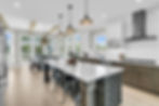 Open kitchen with white island, bar stools, wine rack, and dining room