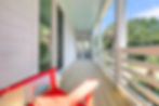 Long wooden porch with white railings, red chair, and light blue ceiling
