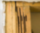 Close-up of a damaged wooden window frame with cracked, termite-eaten boards and peeling white trim.