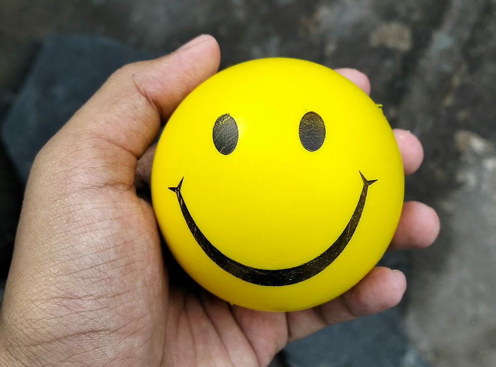 Close-up of a hand holding a yellow smiley-face stress ball, highlighting tactile squeezing for grounding and anxiety relief during moments of stress.