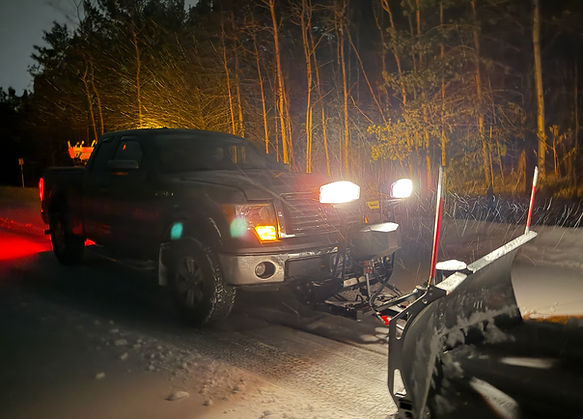 Snow plow truck clearing a driveway at night during snow removal service in Duluth MN