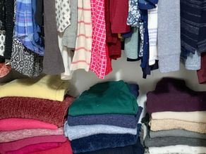 Organized closet. Sweaters folded on shelf clothing hung on clothing rod in organized closet