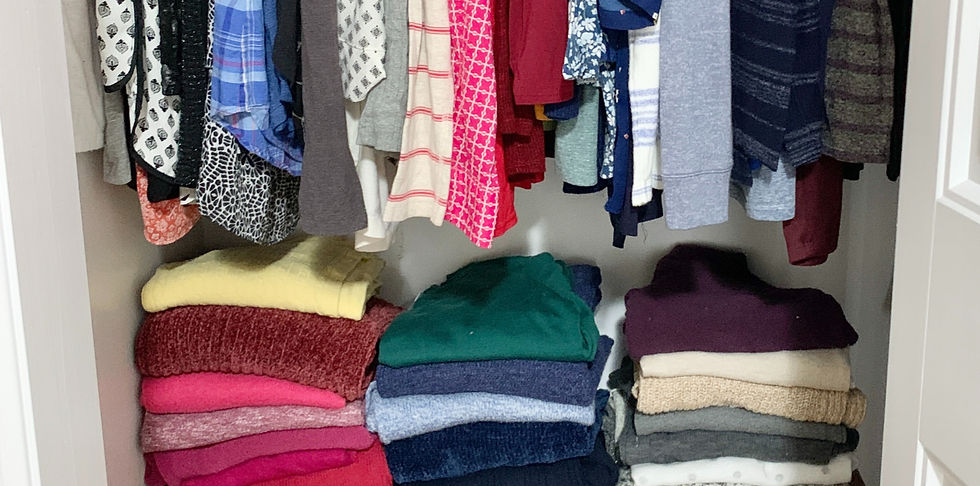 Organized closet. Sweaters folded on shelf clothing hung on clothing rod in organized closet