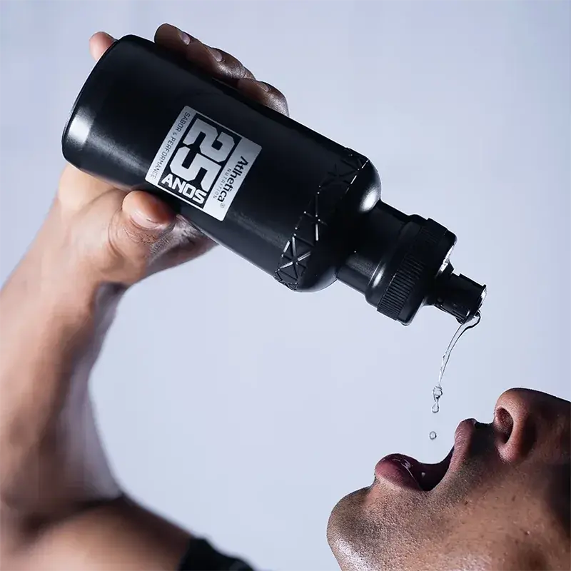 Pessoa bebendo água de garrafa preta com detalhes em branco e cinza, 25 anos.