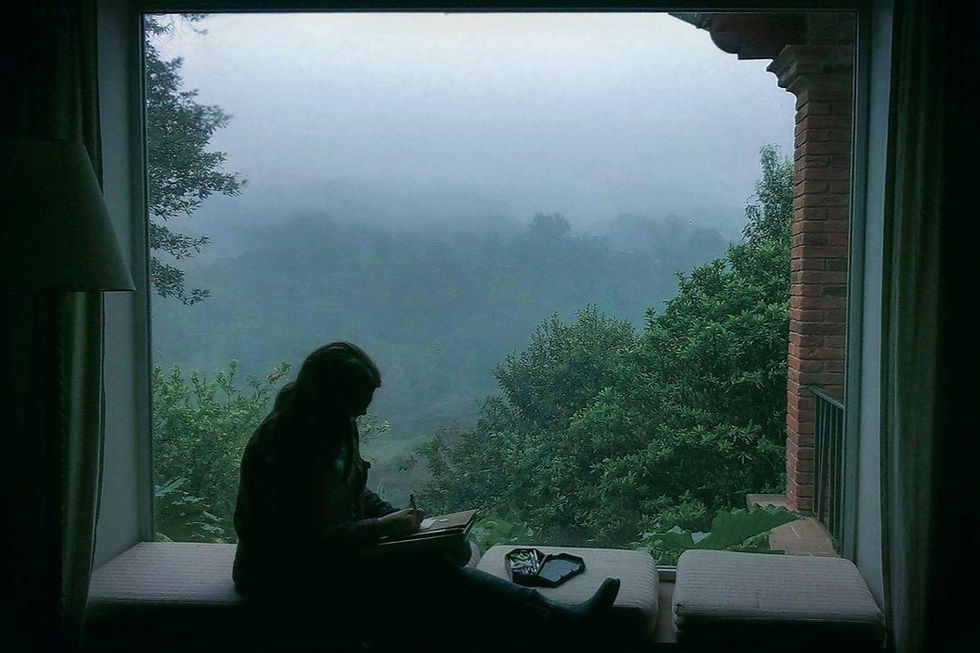 A woman sits by a window, gazing out at the rain—lost in thought, wrapped in the quiet weight of everything she’s been through but couldn’t explain.