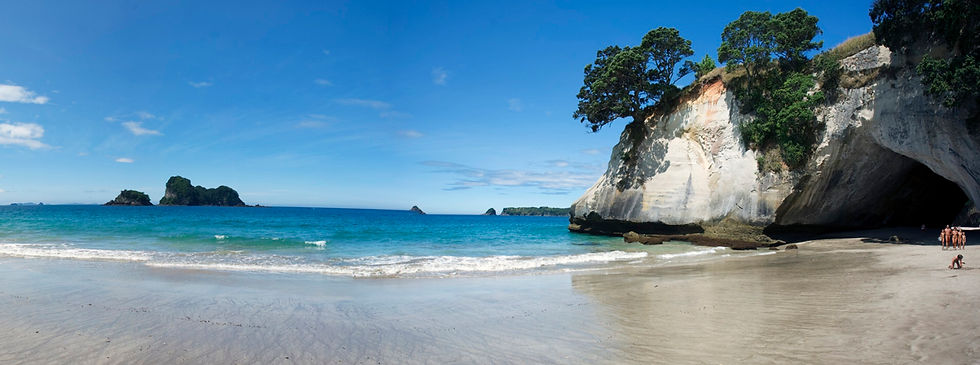 A panoramic shot of Cathedral Cove's famous rock arch and white sand beach in the Coromandel Peninsula, featuring a naturist family in the distance.