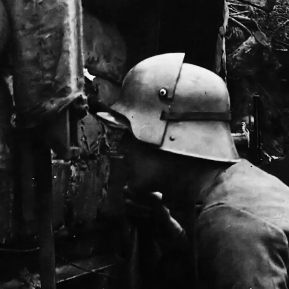 WW1 German soldier wearing a Stahlhelm fitted with a Stirnpanzer brow plate while observing from a trench, period photograph