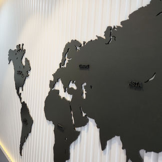 Black world map wall decor placed behind a bed, featuring the inspiring quote 'To travel is to live.' The sleek, minimalist design adds a modern touch to the bedroom, perfect for travel enthusiasts looking to bring a sense of adventure and wanderlust into their space.