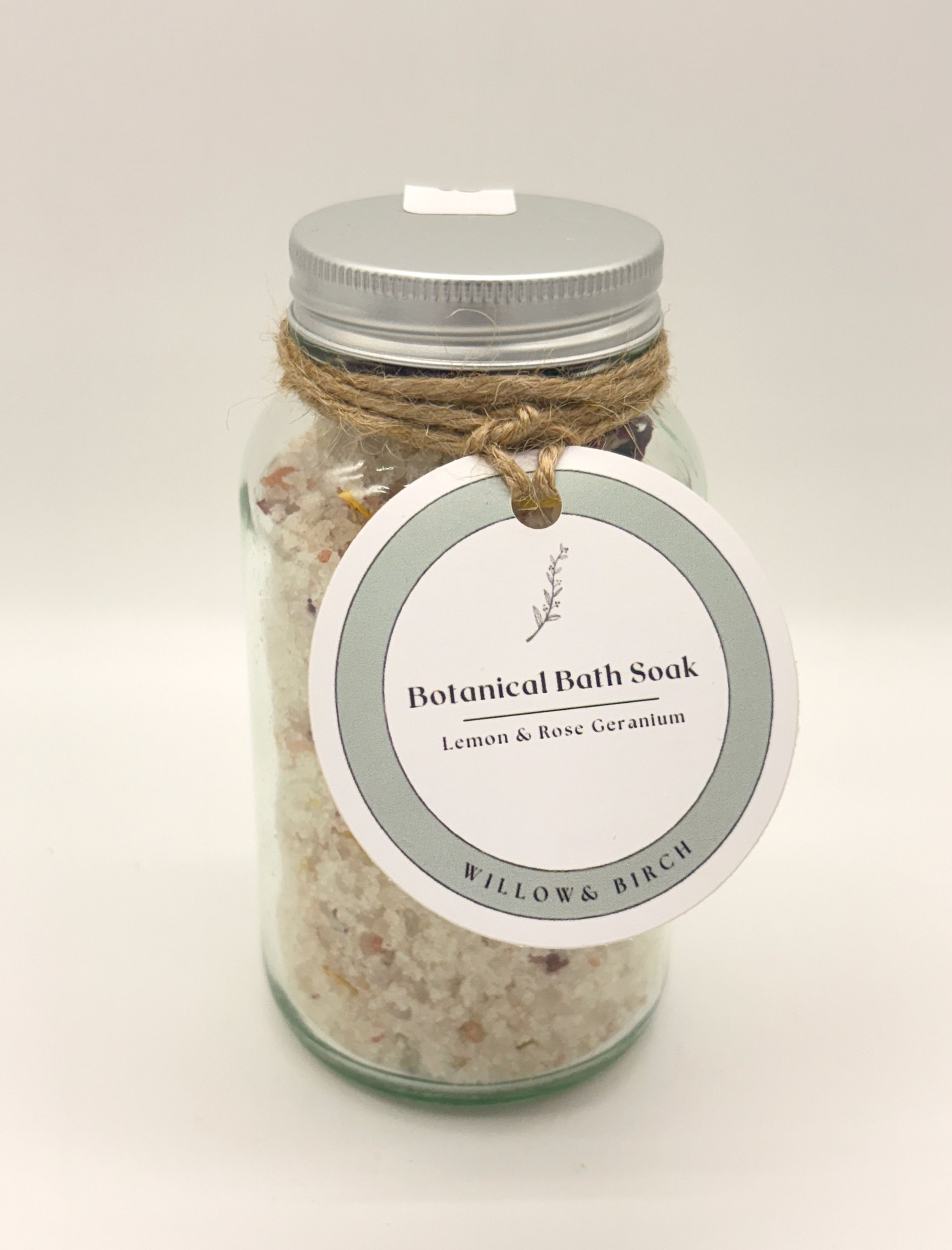 Clear glass jar with silver lid showing bath salts inside with rose petals