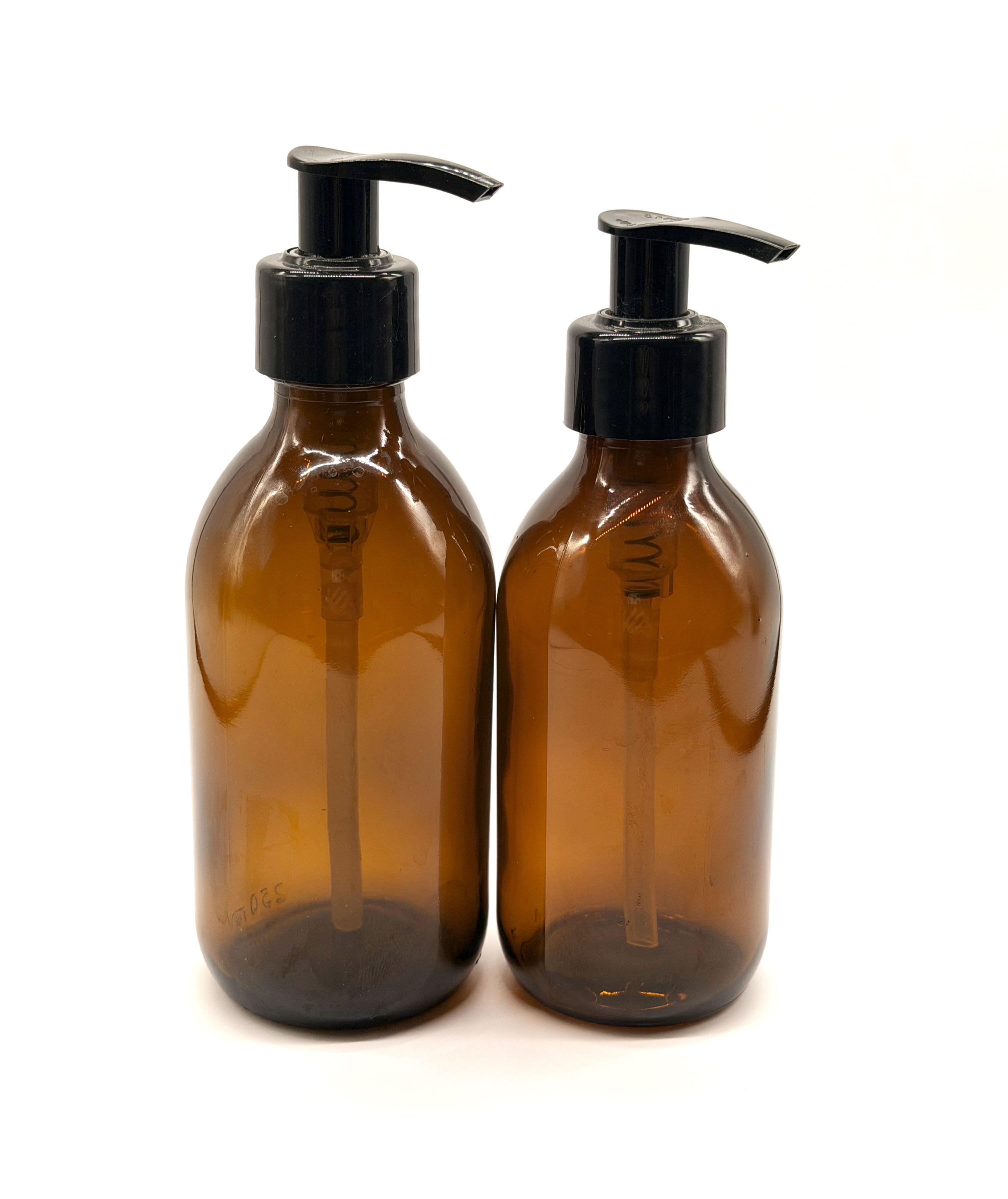 two empty amber glass bottles with black pump lids standing side by side one slightly larger than the other.