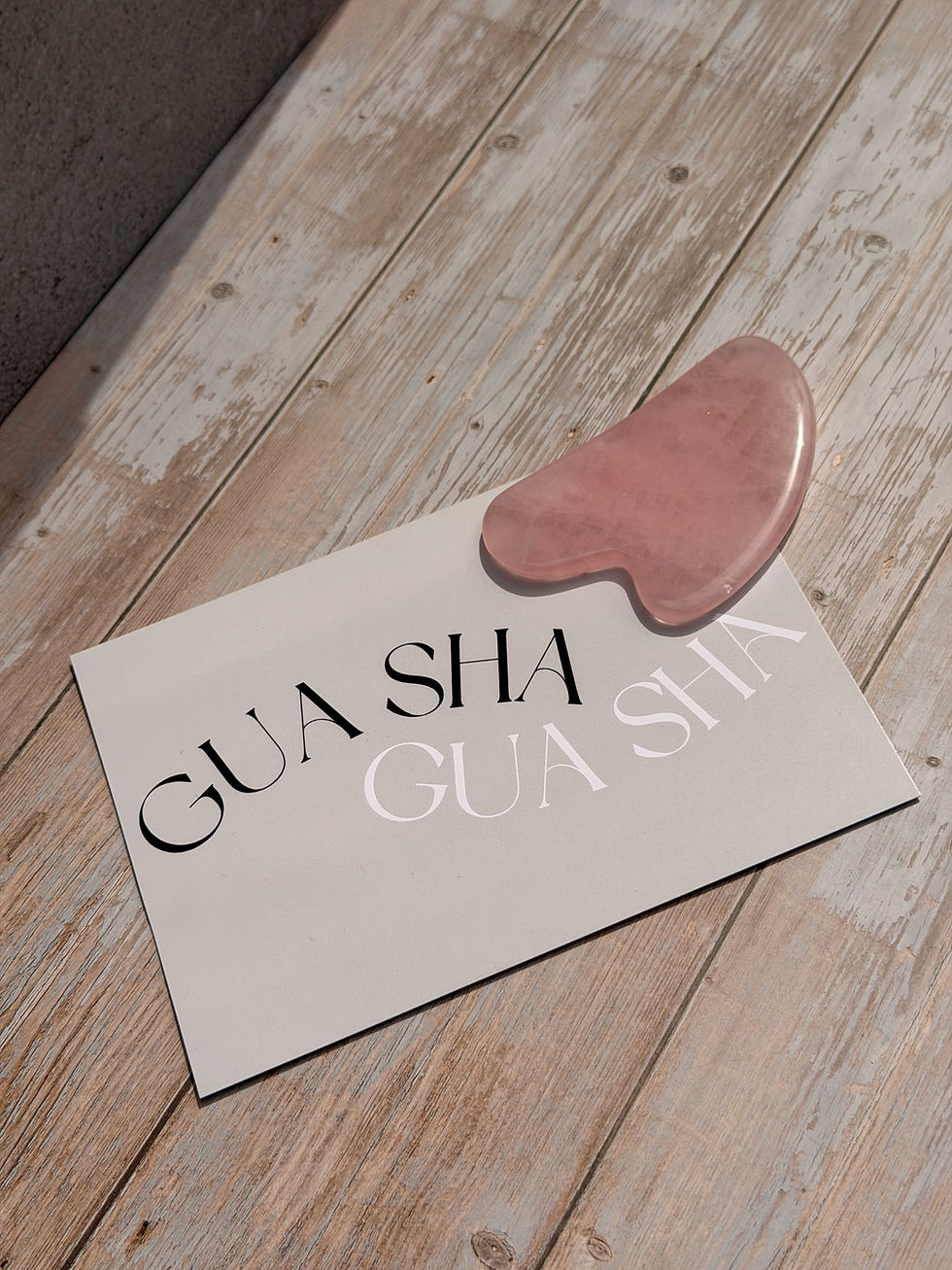 A pink rose quartz gua sha massage stone lying on light wood surface with a pale green instruction card lying next to it