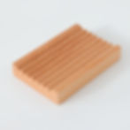 A light coloured wooden soap dish in a rectangle shape.  the top of the dish has grooves etched in the top to allow water to run down them.