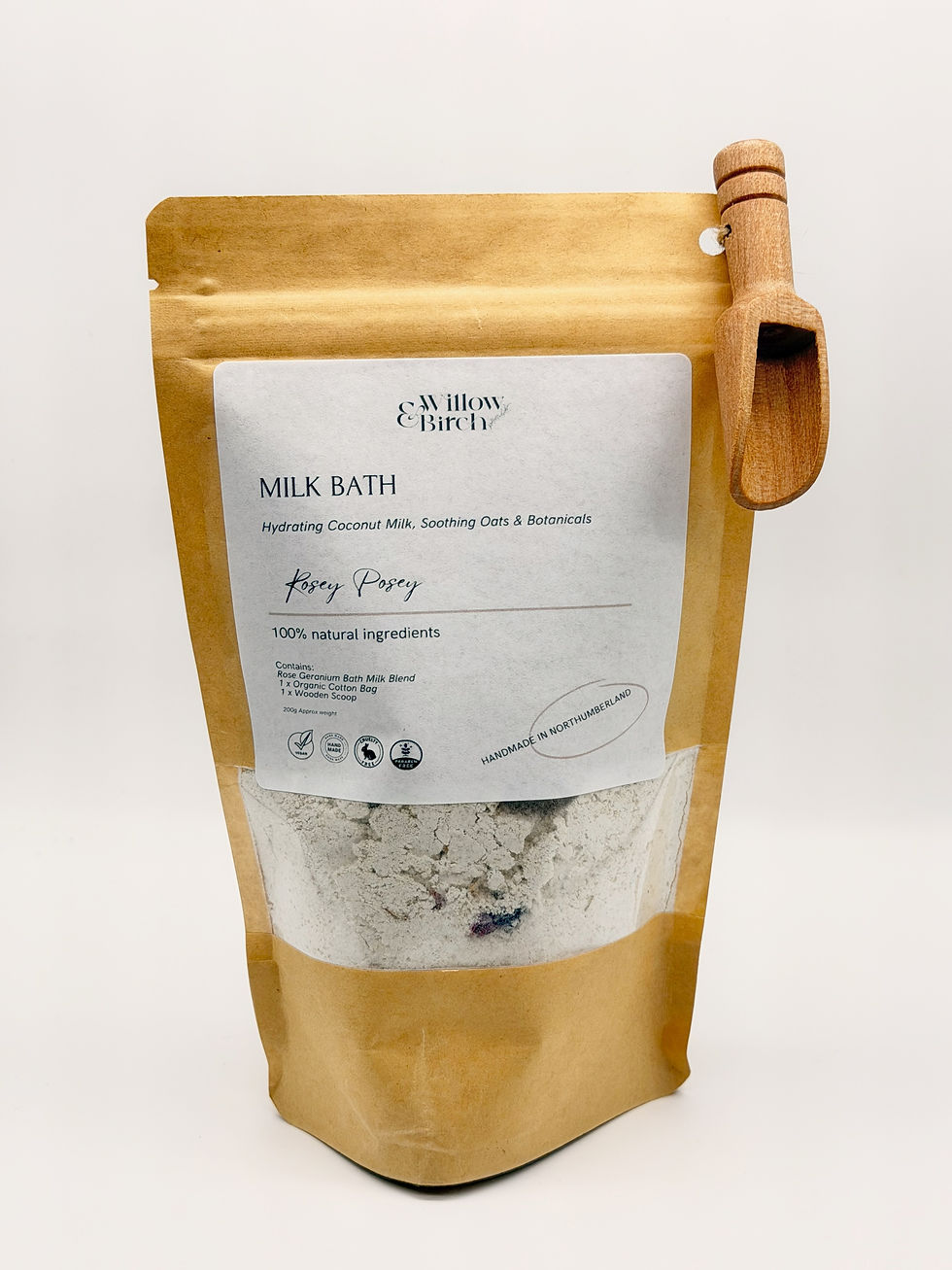 A brown pouch bag with clear window showing bath milk inside, a small wooden scoop is attached to the corner of the bag