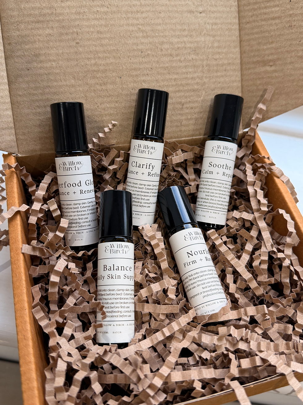 Five mini brown glass rollerball bottles in brown box with brown paper stuffing
