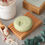 Thumbnail: Round pale green coloured shampoo bar lying on wooden soap dish. There is some bath salts scattered in front of the soap dish along with a  small wooden scoop.