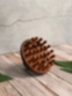 A wooden scalp massager lying on a light wooden surface with green leaves nearby.