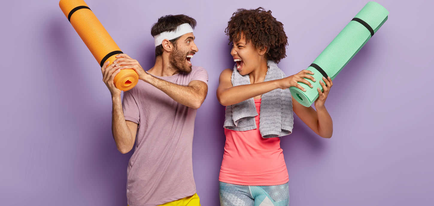 funny-multiethnic-woman-man-have-fun-gym-fight-with-rolled-up-karemats.jpg