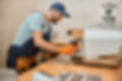 Man in a blue cap and overalls, smiling while fixing a coffee machine