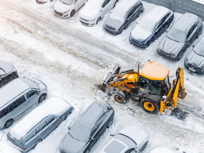 Aerial view of tractor loader machine plowing a parking lot covered in ice and snow.
