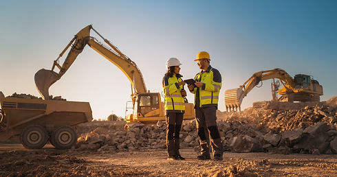 Construction workers reviewing plans at an active excavation site with excavators and heavy equipment
