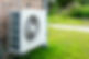 Outdoor air conditioner unit fixed to a brick wall, surrounded by lush green grass and trees