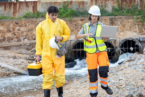 Environmental Engineers in PPE Suits Inspecting Wastewater Discharge from Industrial Pipe