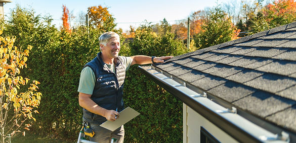 Un homme inspecte le toit d'une maison, debout sur une échelle.