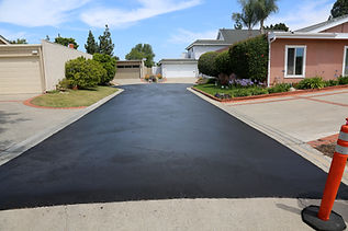 Freshly paved black asphalt driveway leading to two white garages