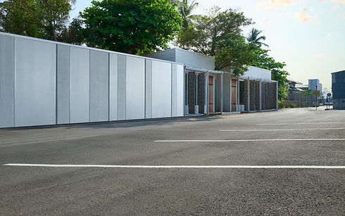 Empty parking lot bordered by modern white buildings and lush green trees under a clear sky