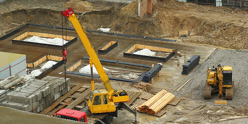  construction site with a yellow crane lifting materials near concrete blocks and wooden planks