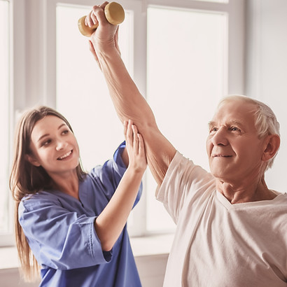 Young female therapist assists an older man lifting a small dumbbell in a bright room