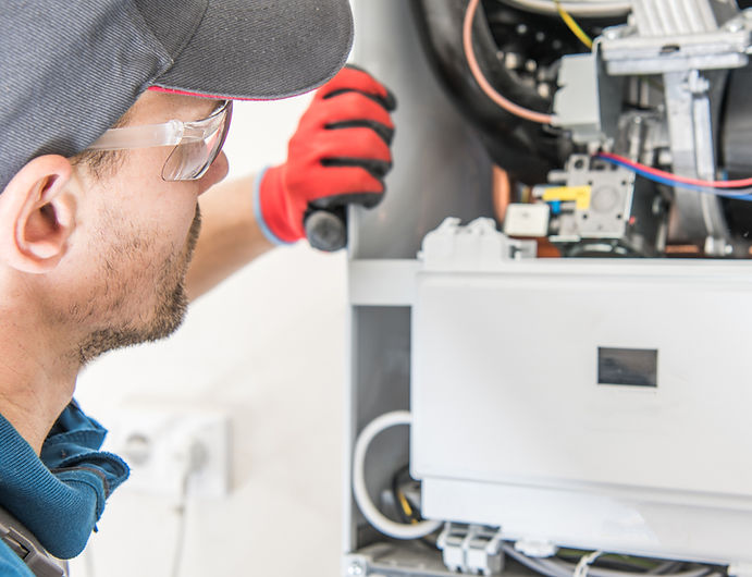 A technician in safety glasses and red gloves inspects a furnace