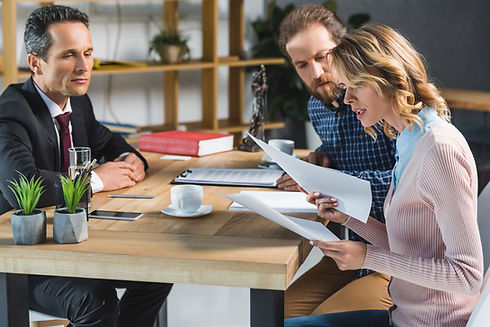 Three professionals sitting at a wooden table in an office, reviewing documents
