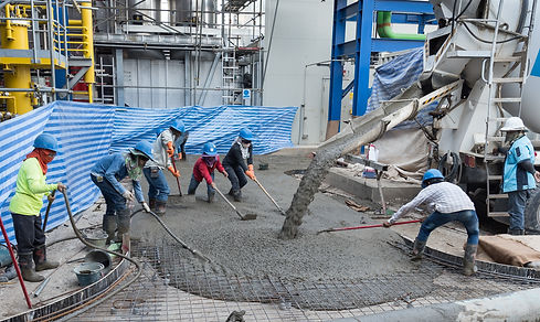 Construction workers in hard hats are pouring concrete from a mixer into a rebar frame