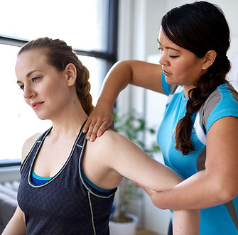 Two women in a bright room; one gives the other a shoulder massage