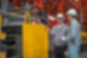 Two male factory engineers wearing hard hats discuss machinery on a busy manufacturing floor