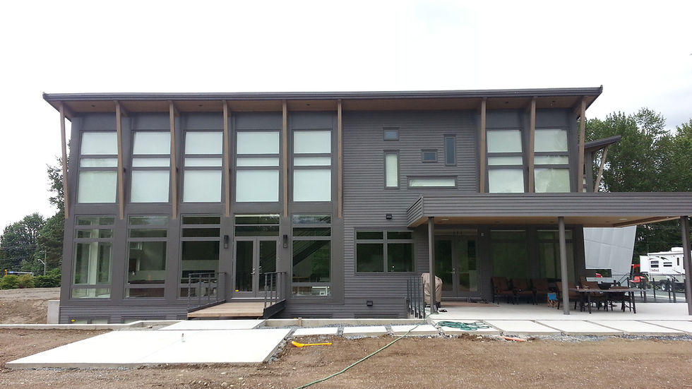 Modern gray two-story house with large windows, surrounded by concrete slabs and a patio area