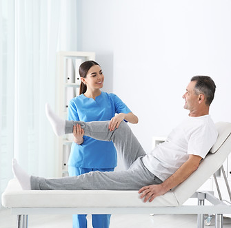 A physical therapist in blue scrubs assists a smiling man