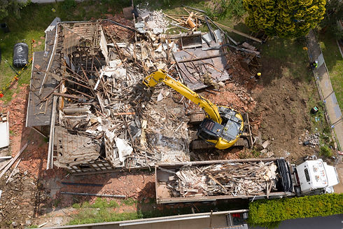 Overhead view of a construction site with a yellow excavator demolishing a house