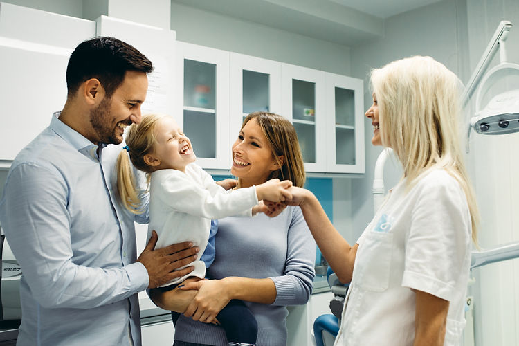 A happy family of three, including a child, interacts warmly with a smiling dentist in a modern dental office